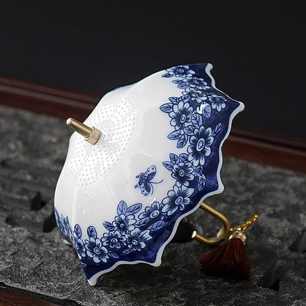 An elegant ceramic umbrella tea strainer resting on a white teacup