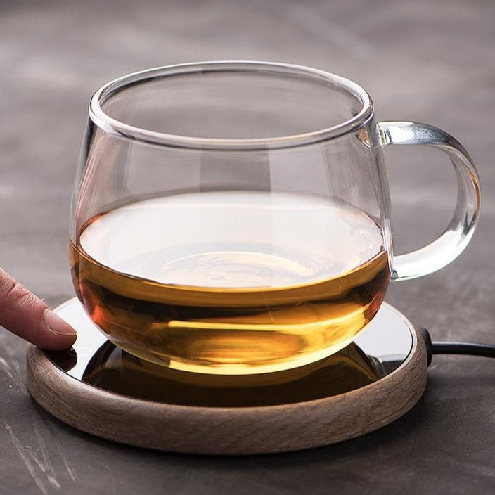 A stylish white mug warmer coaster sitting on a wooden table next to a plant