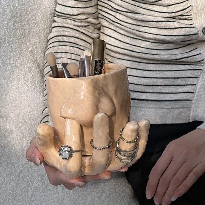 A white ceramic mug with a unique base sculpted into the shape of a hand.