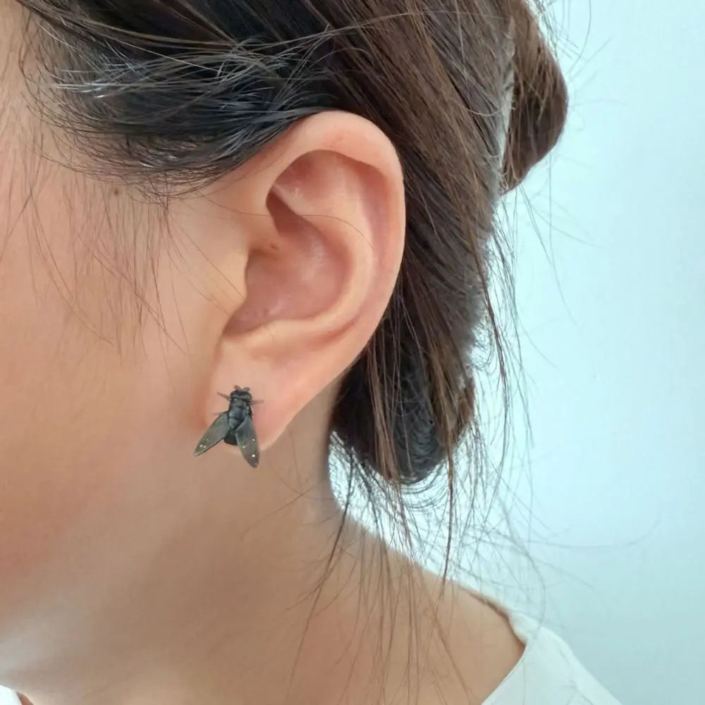 Detailed close-up of the realistic fly design on the abstract earrings